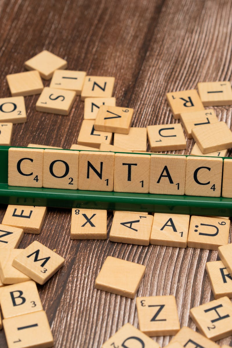 Scrabble tiles spelling 'CONTACT' on a wooden surface with scattered tiles around.